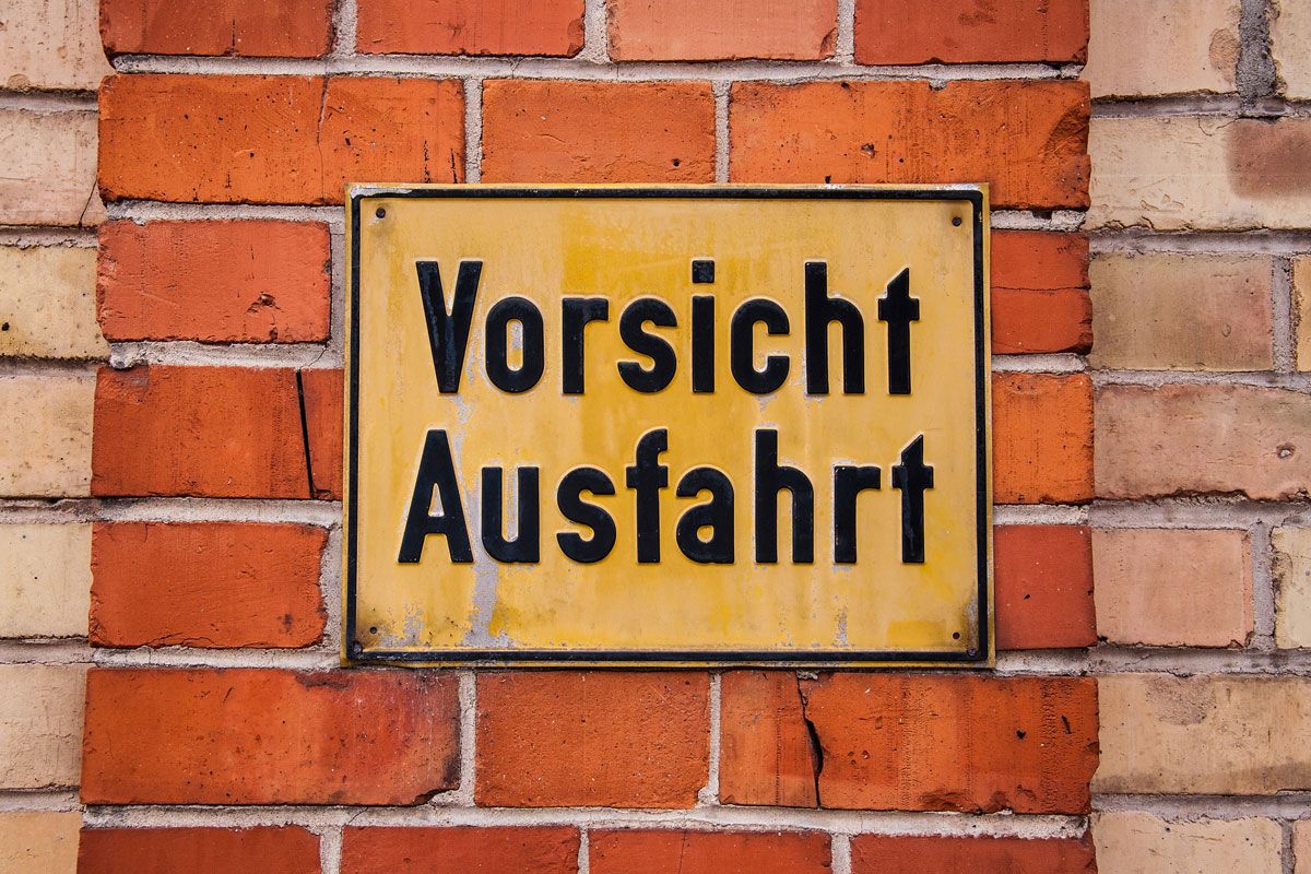 Gelbes Schild an einer Wand mit Aufschrift "Vorsicht Ausfahrt"