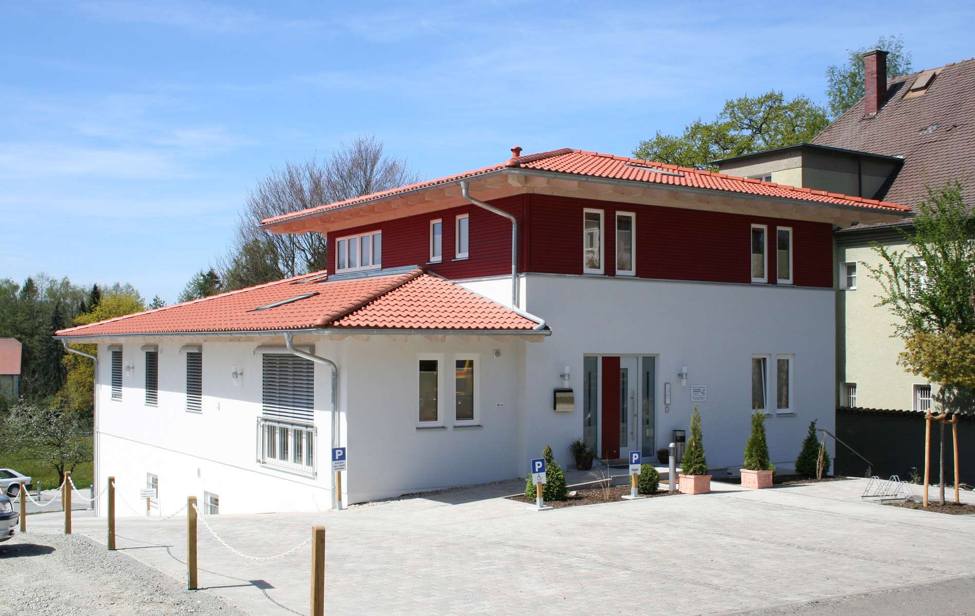 Moderne Zahnarztpraxis aus Holz in mediterranem Baustil und einer Mischfassade aus mineralischem Außenputz und rot gestrichenen Fichtenholzfassade