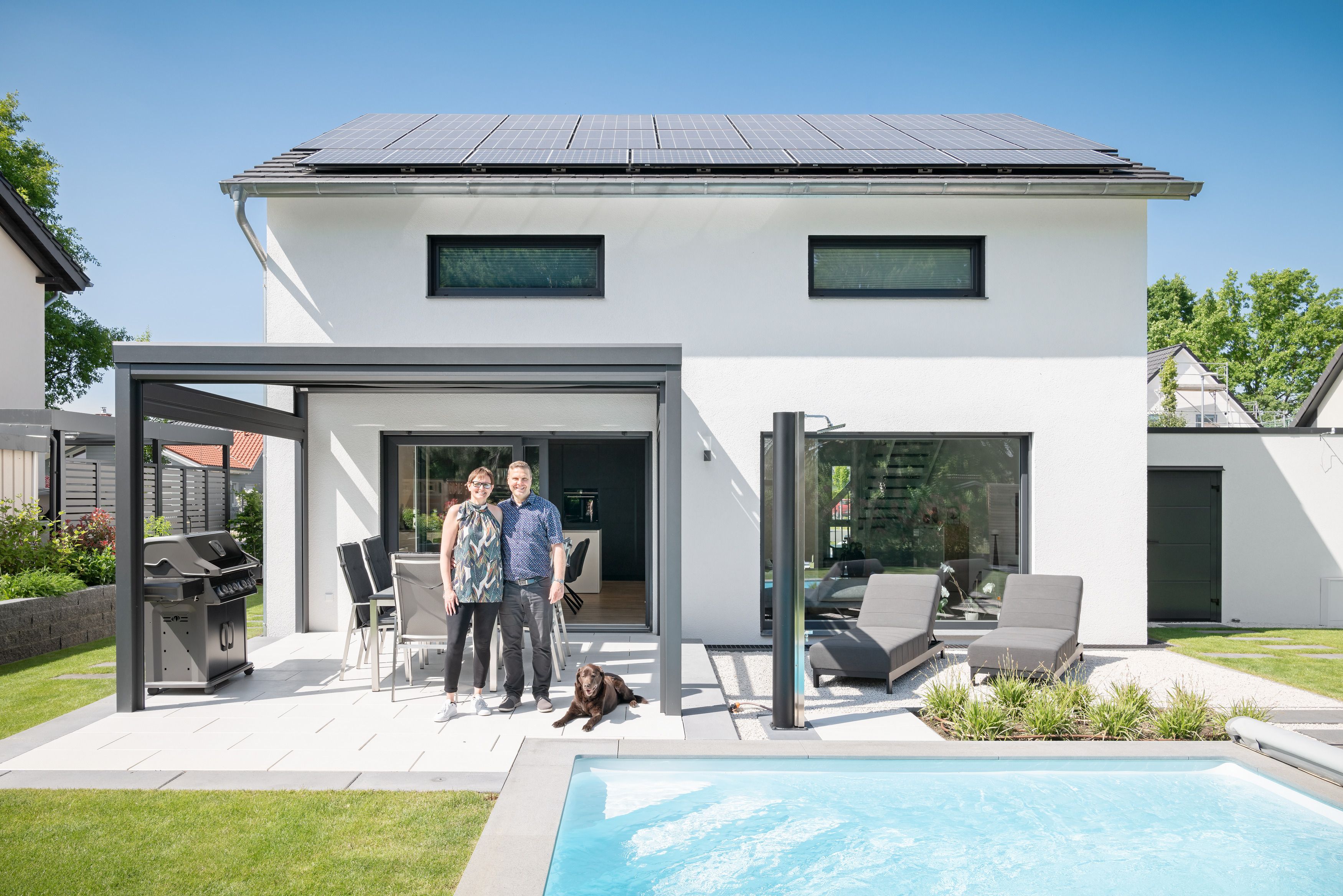 Bauherren auf der Terrasse ihres Einfamilienhauses mit Garten und Pool