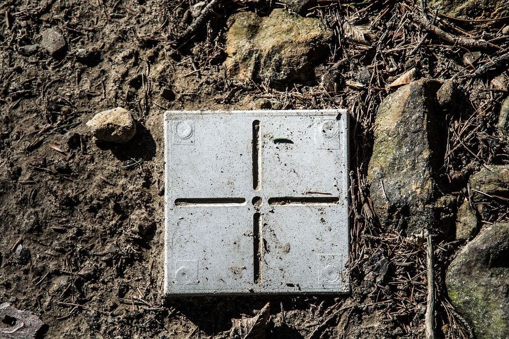 Grauer Messpunkt im Garten als Grundstücksbegrenzung