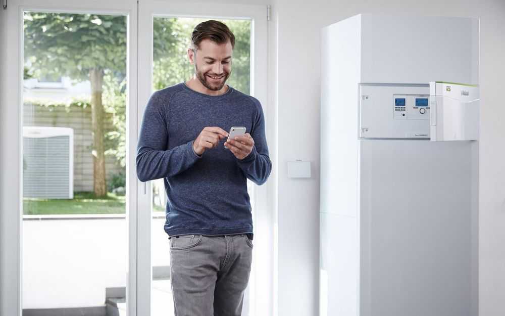 Mann steht in der Küche und guckt auf sein Smart Phone